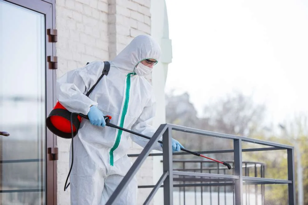 Disinfection specialist in protective suit spraying disinfectants to sanitize residential room during pandemic